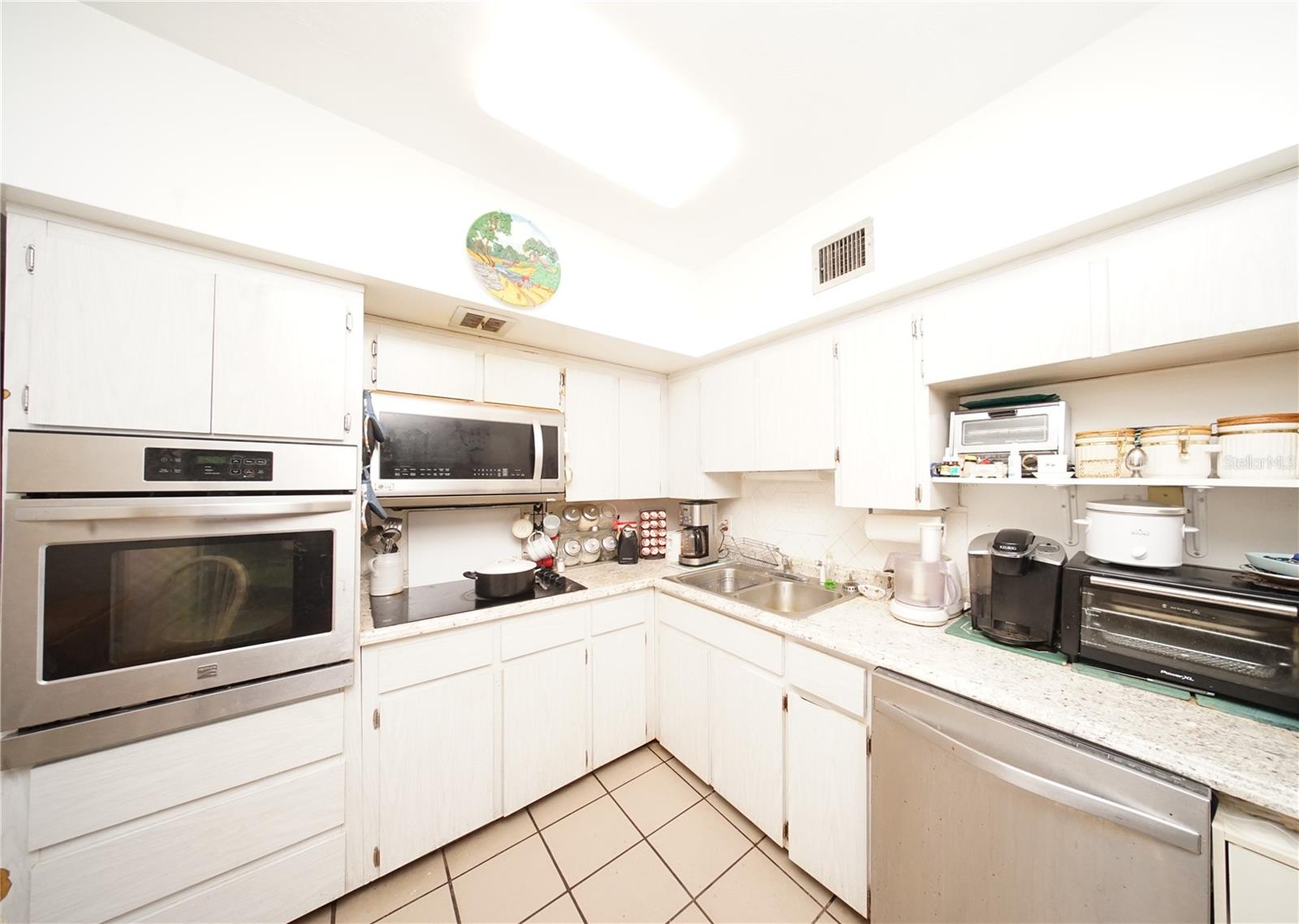 Kitchen with Ceramic Tile Flooring, Newer Stainless-Steet Dishwasher, Newer Stainless-Steel Microwave, Newer Stainless-Steel Built-in Oven and Sliding Glass Door that open to Spacious Florida Room