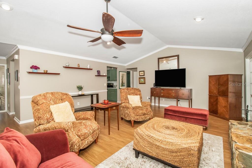 As you continue inside the home, you will notice one of the many standout features of this home is the spacious living room with cathedral ceilings, wood-burning fireplace, and two sets of French doors that lead out to the large, screened pool area.