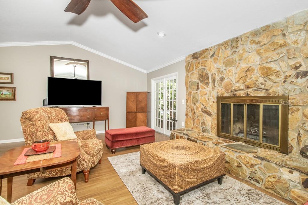 As you continue inside the home, you will notice one of the many standout features of this home is the spacious living room with cathedral ceilings, wood-burning fireplace, and two sets of French doors that lead out to the large, screened pool area.