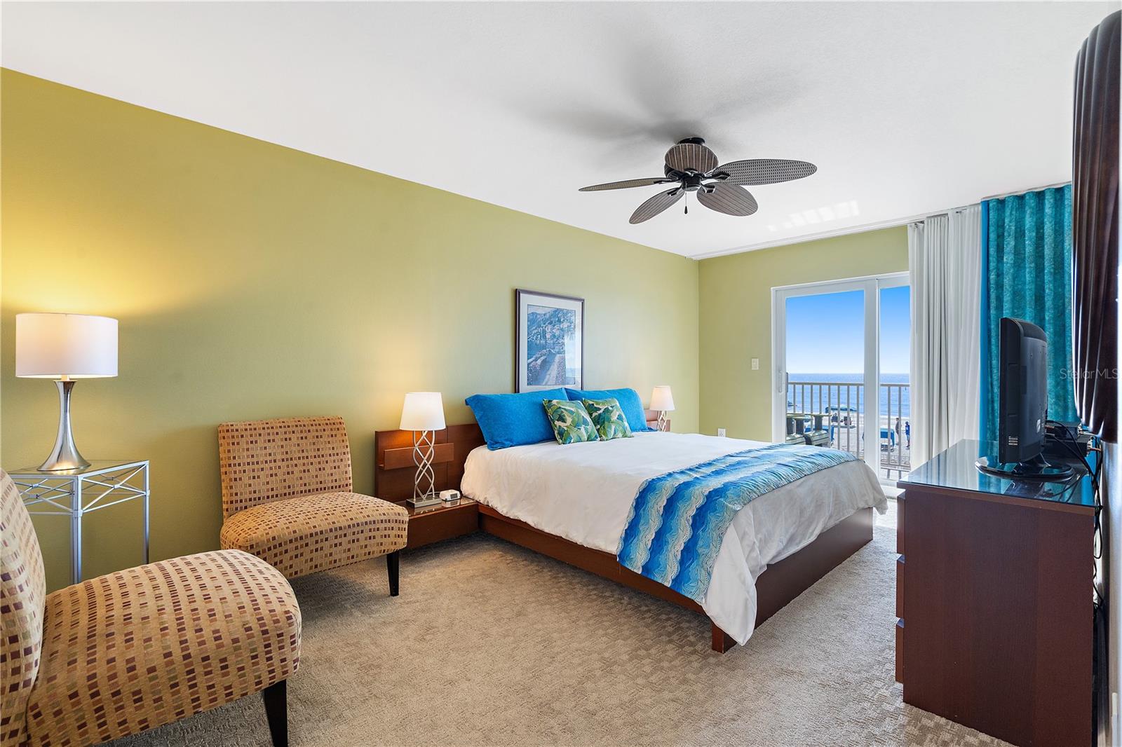 The spacious primary bedroom features a sitting area, a balcony with a water view, sheers, and blackout curtains. The carpet was chosen for maximum comfort, contributing to a memorable vacation experience.