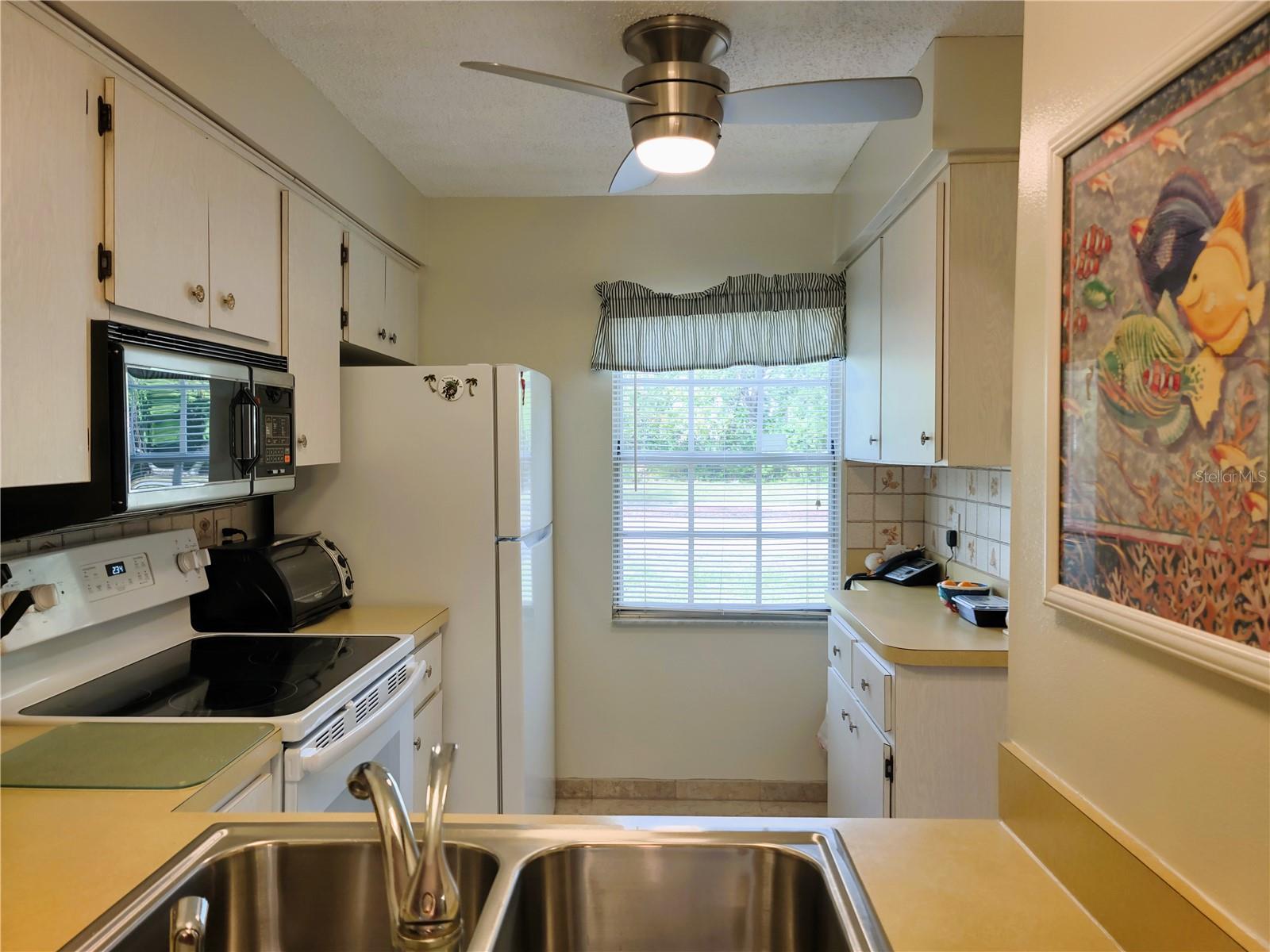 Kitchen features stainless steel sink, glass top range, microwave, new ceiling fan and refrigerator.