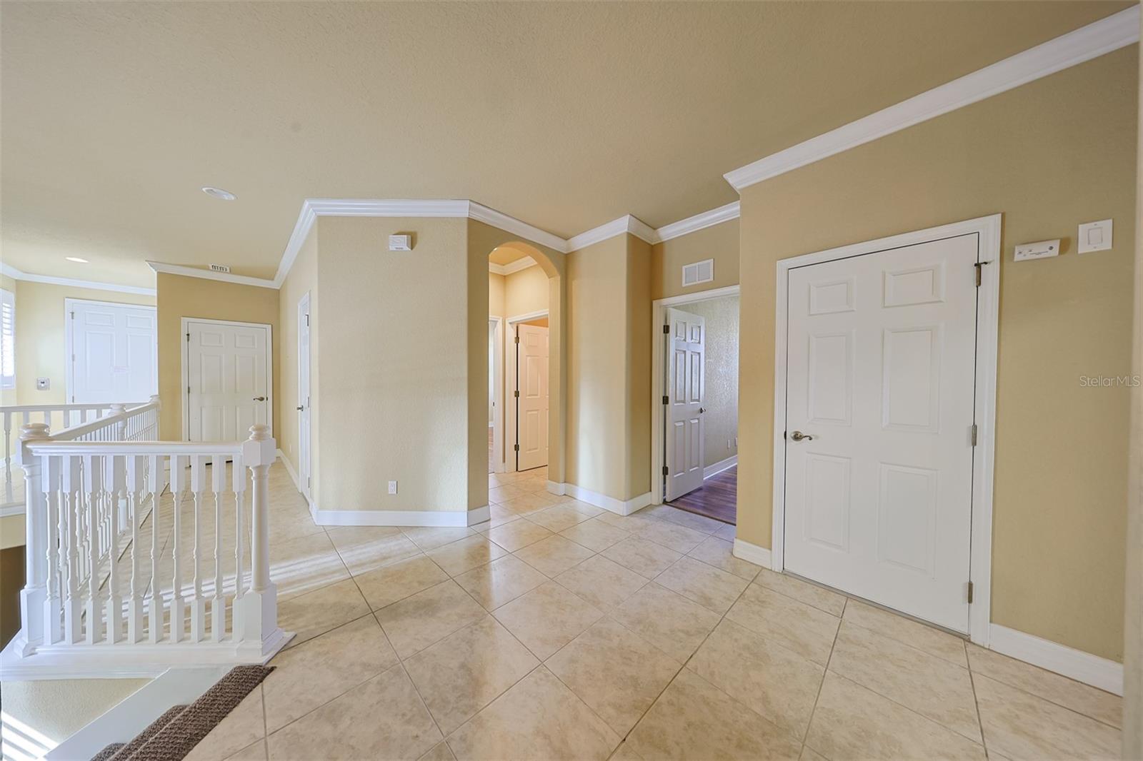 View of the foyer entrance and split floor plan bedrooms and guest bath to the right. In the far back left is the private elevator that comes from the garage. Notice the attractive crown molding that match the handrail.