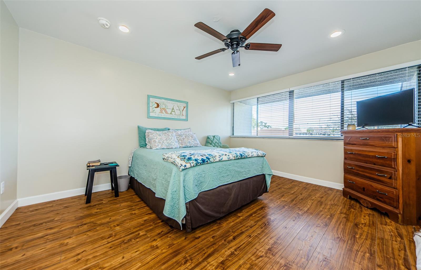 Spacious bedroom has ceiling fan, recessed lighting, wall of windows and beautiful plank laminate flooring