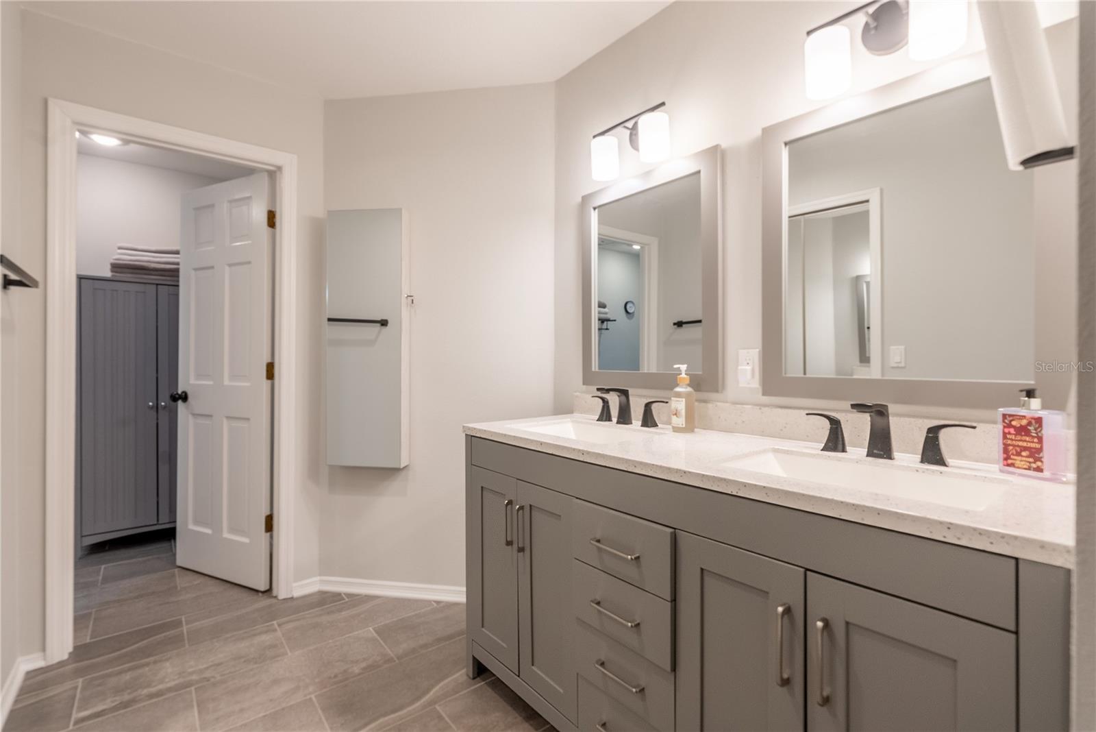 The primary bathroom has a double vanity, and a mirrored jewelry cabinet affixed to the wall