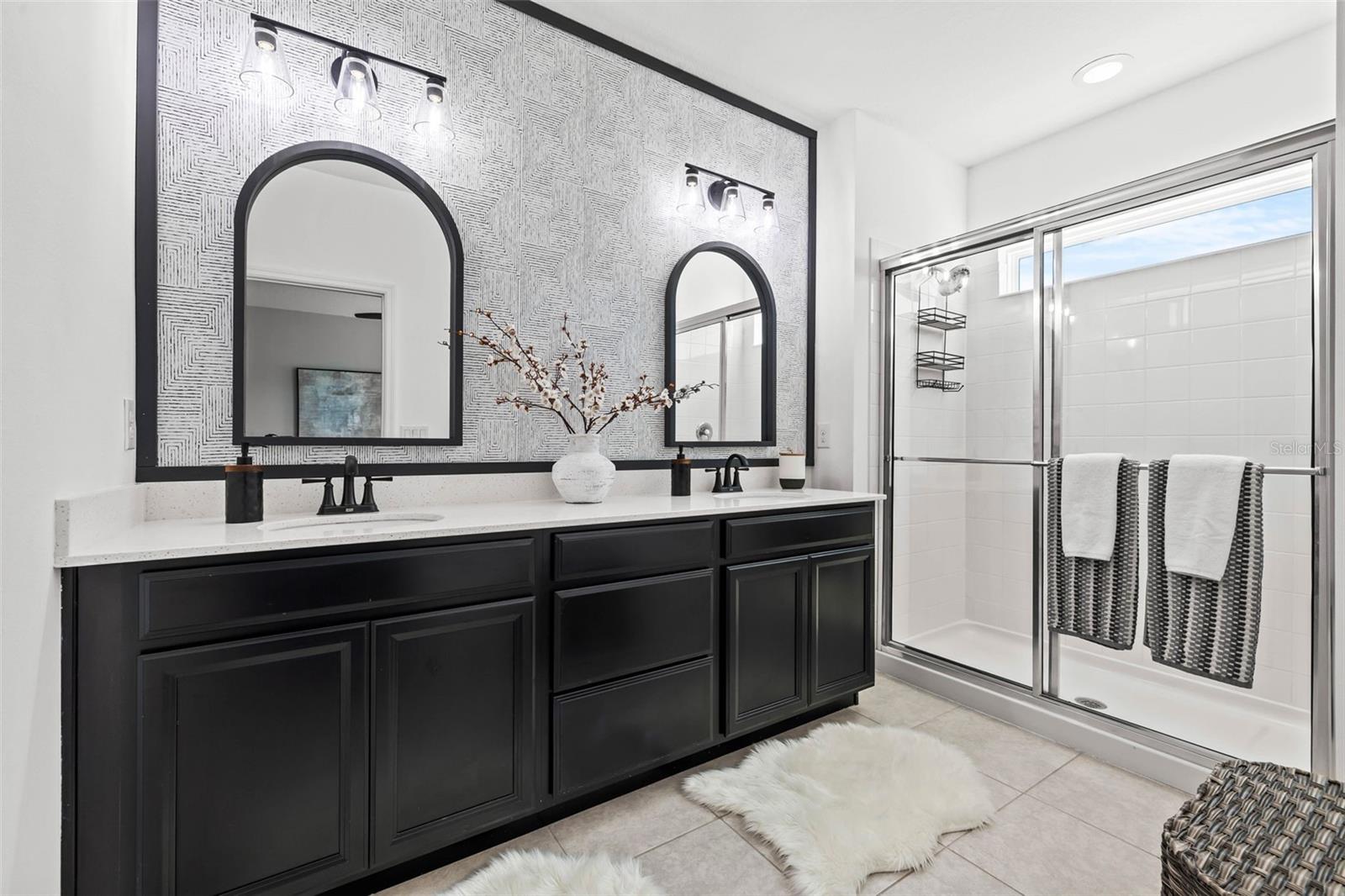 Primary Bathroom featuring private water closet, custom mirrors, faucet upgrades, upgraded light fixtures, tiled shower, and design wall papered wall for a modern  aesthetic