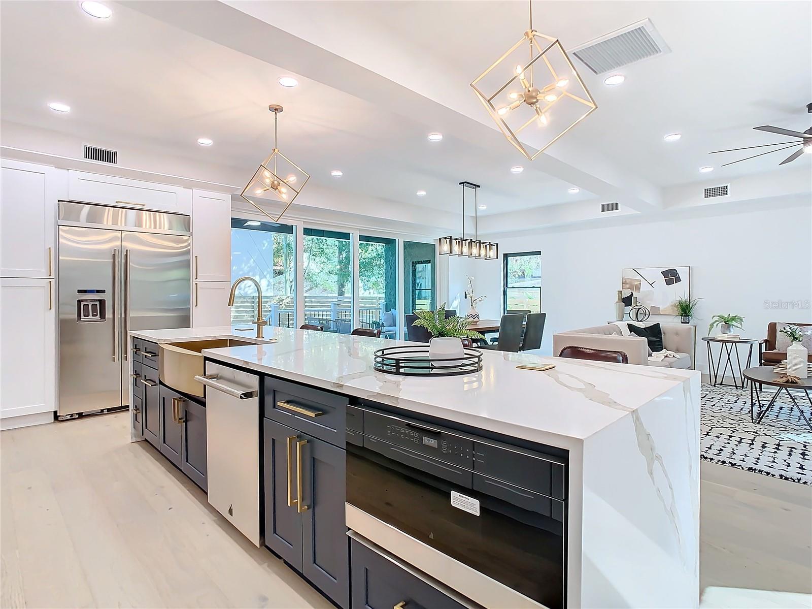 Chef kitchen features two-tone cabinets, Jenn-Aire double ovens, below island microwave, two-tone aoft close cabinets with luxury hardware, lighting, and vanishing USB Charging set inside quartz counters