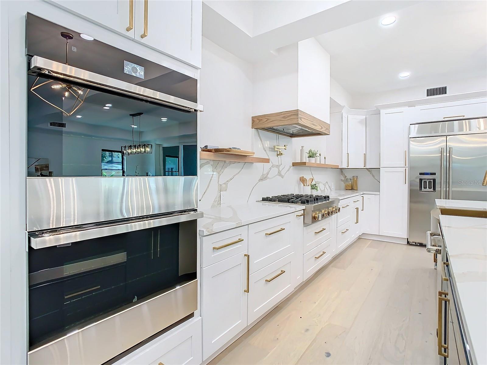 Gourmet Kitchen with Two-Tone Cabinets, Jenn-Aire Double Ovens, Below Island Microwave, Two-Tone Soft Close Cabinets with luxury hardware, lighting, and Retracting USB Charging Stations set inside quartz counters