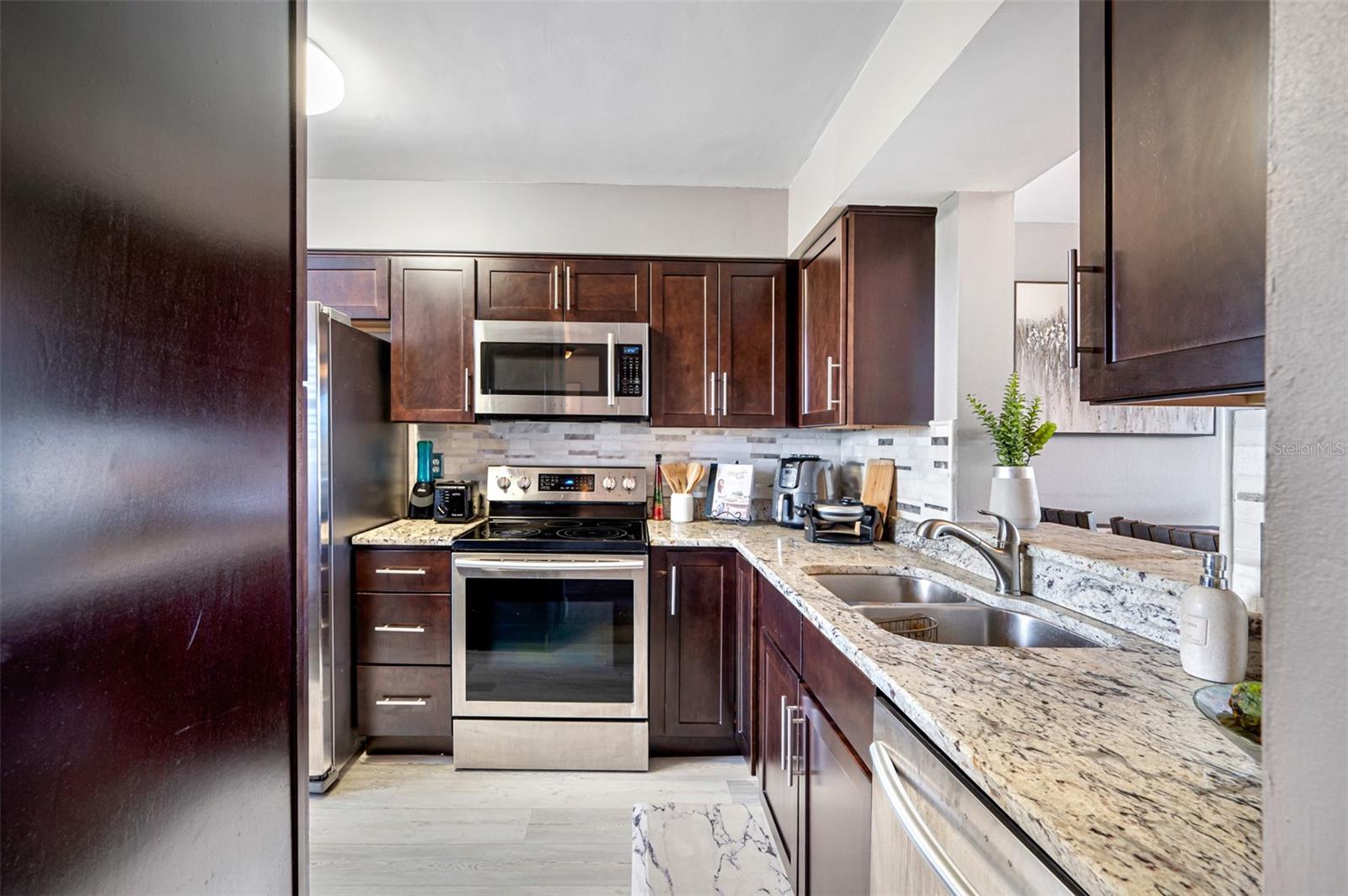 Kitchen with solid wood cabinetry, granite countertops, modern design tile backsplash, and luxury vinyl flooring.