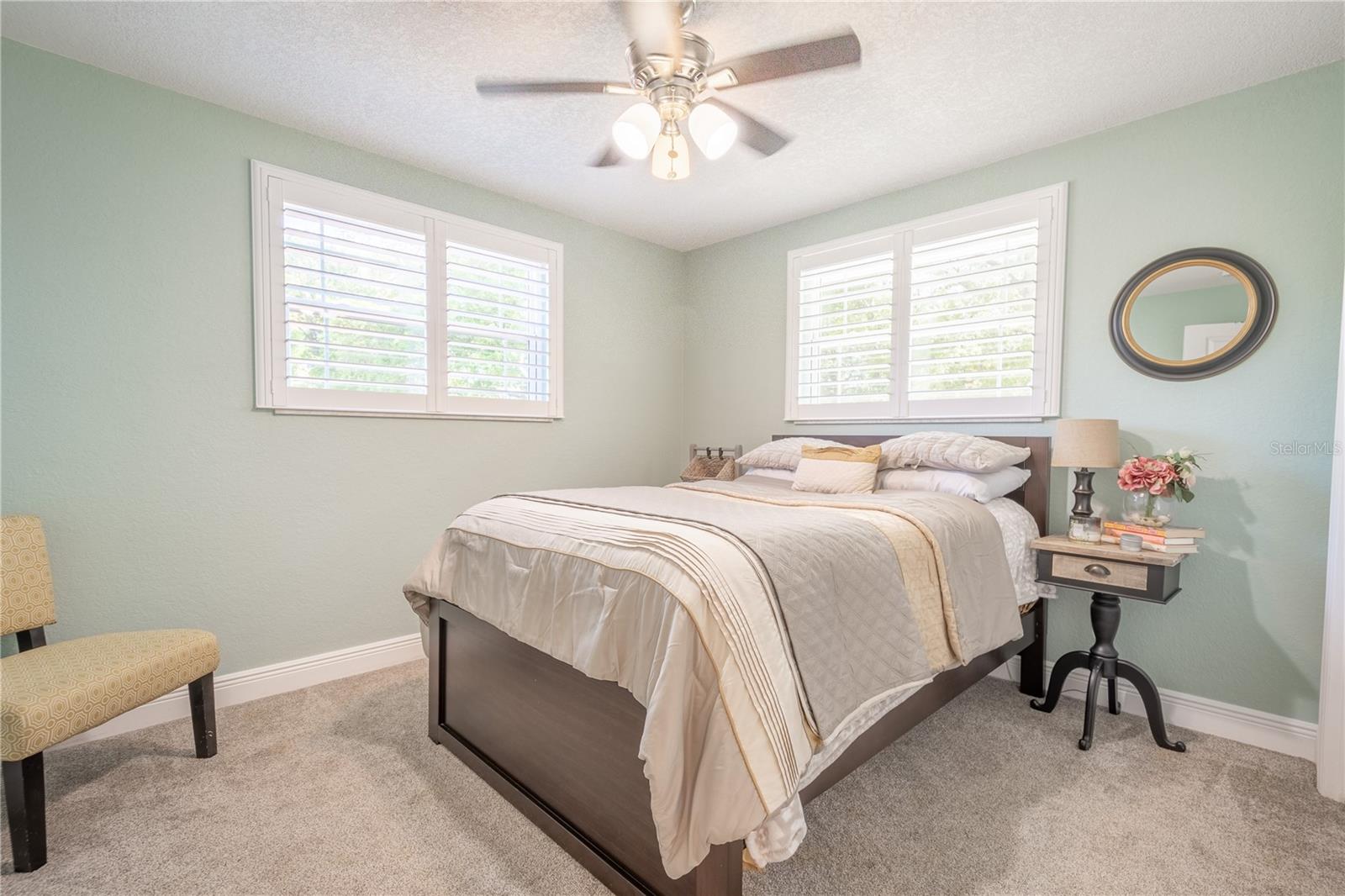 Bedroom 5 features neutral tones, plush carpet, plantation shutters, a ceiling fan and built-in closet.
