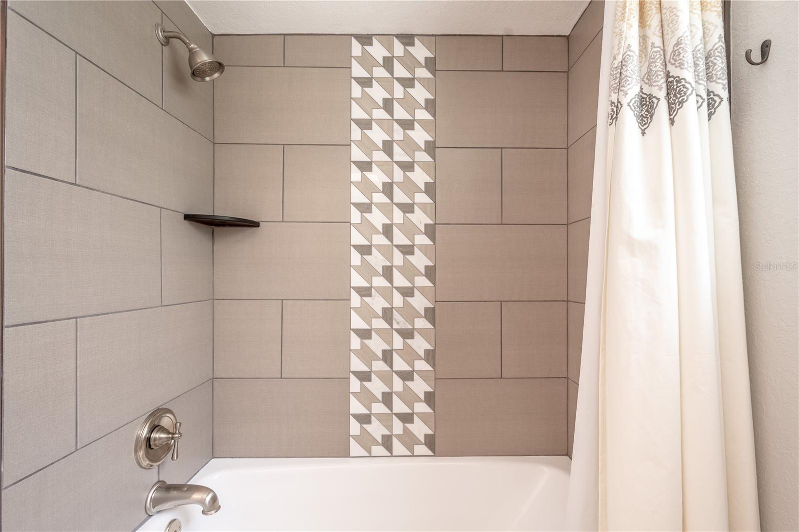 A tub with shower with artistic accent tile in the upstairs full bath.