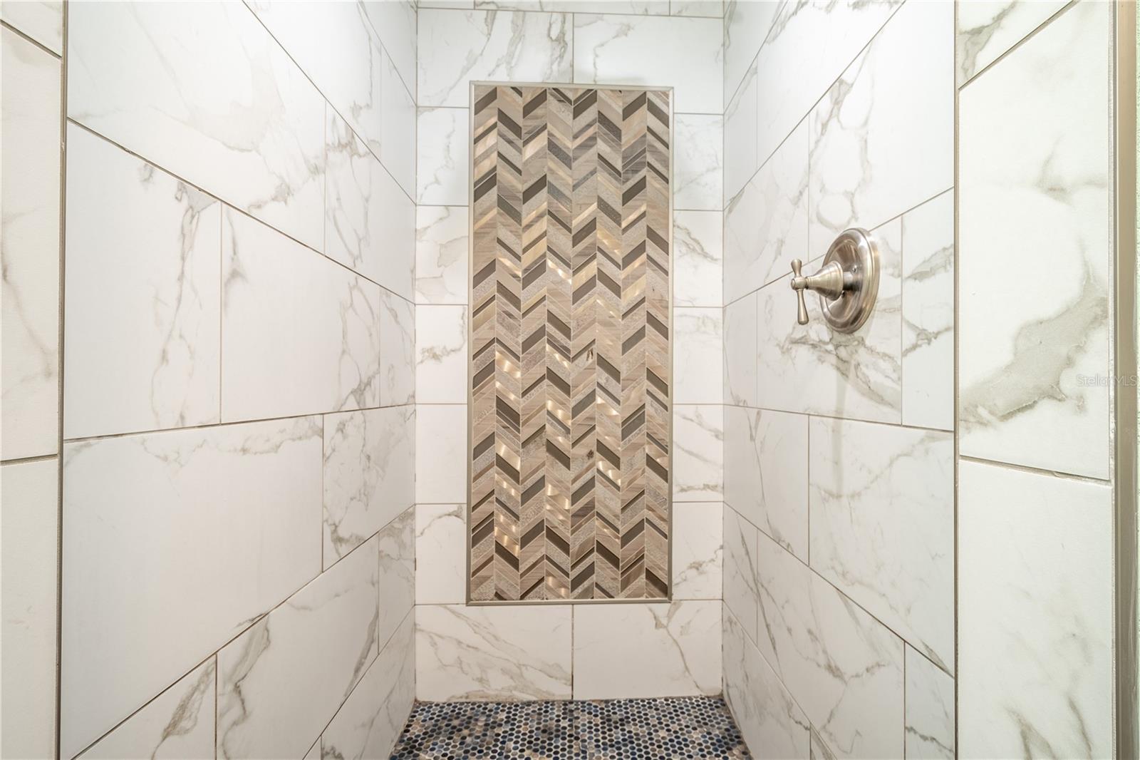 The primary ensuite features a walk in shower with artistic tile accents.