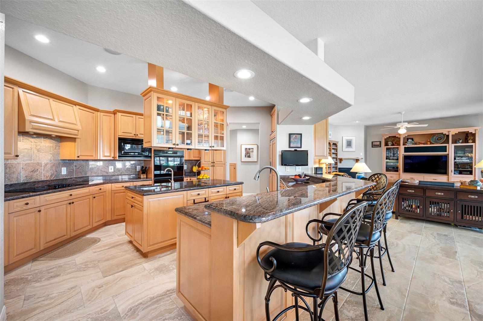 Kitchen with custom wood cabinetry, granite counter tops and backsplash, and expansive breakfast bar