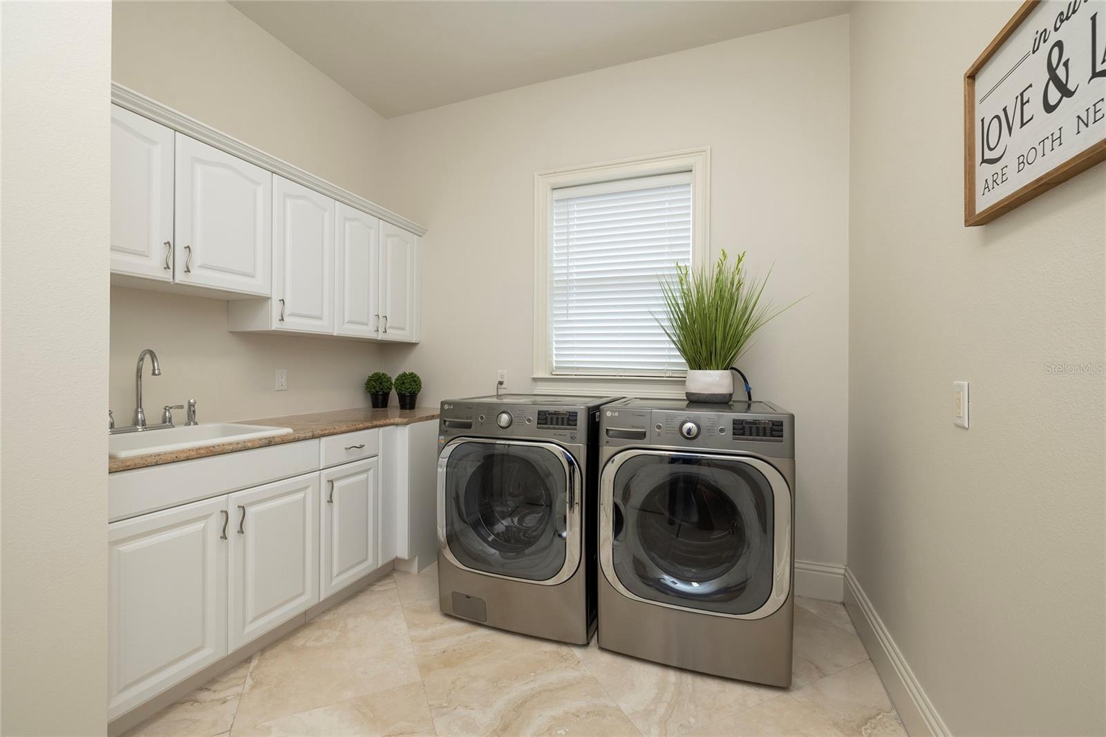 Laundry room with laundry shoot from second floor, utility sink, storage cabinets, and closet.