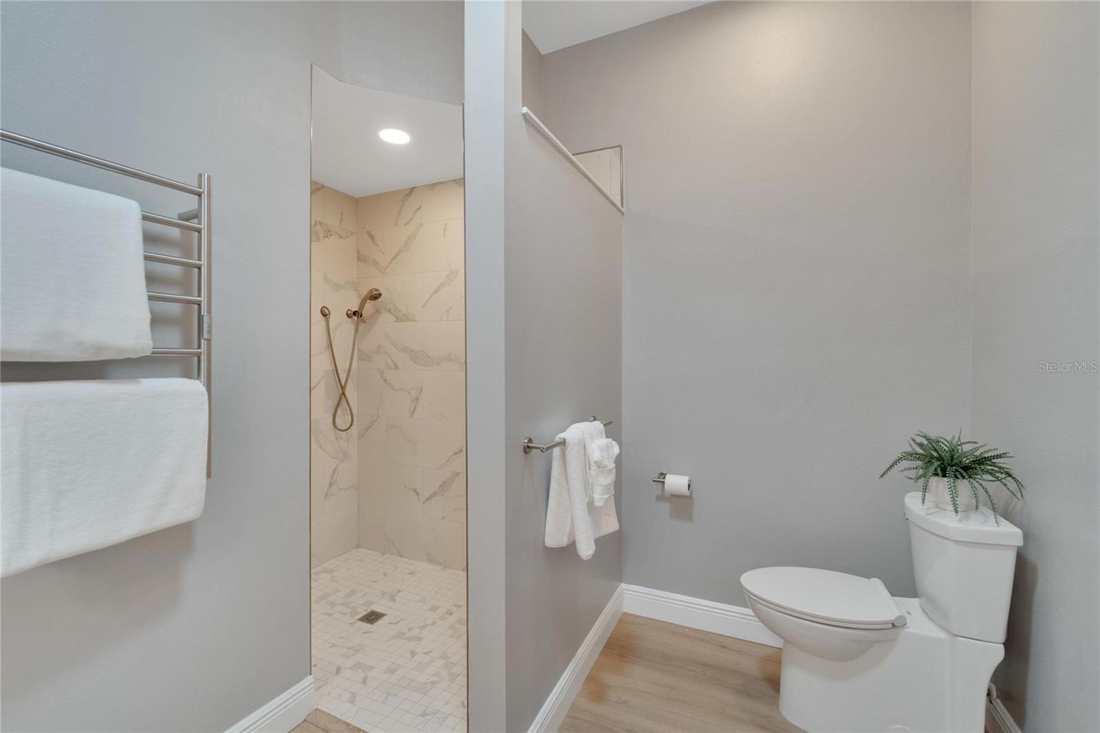 Hard-wired towel warmer, walk-in tiled shower with multiple shower heads, separate toilet area, freshly painted
