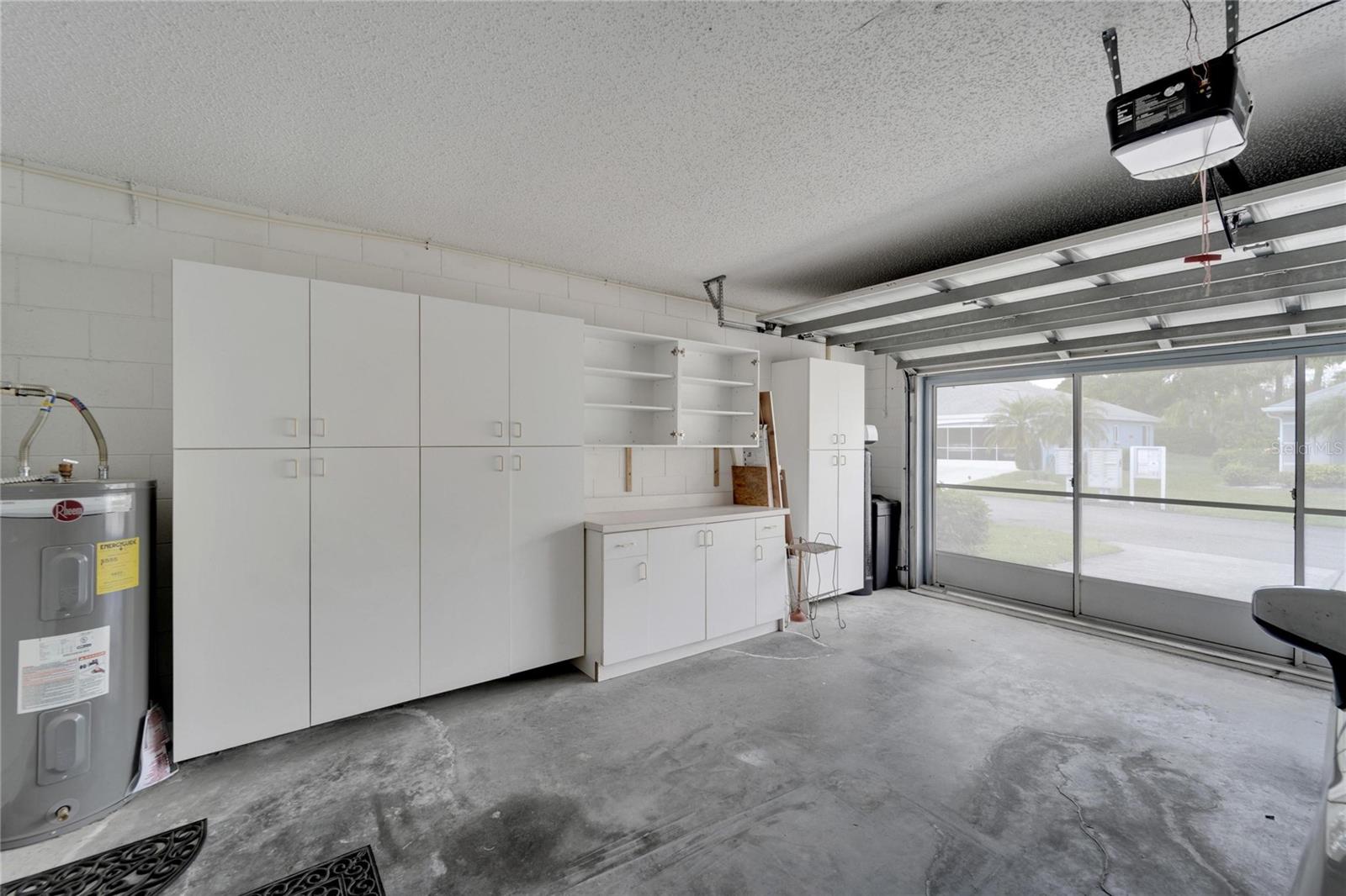2 Car garage with remote control garage opener, with sliding screen doors and a wall full of cabinetry, as well as a countertop for small household projects.