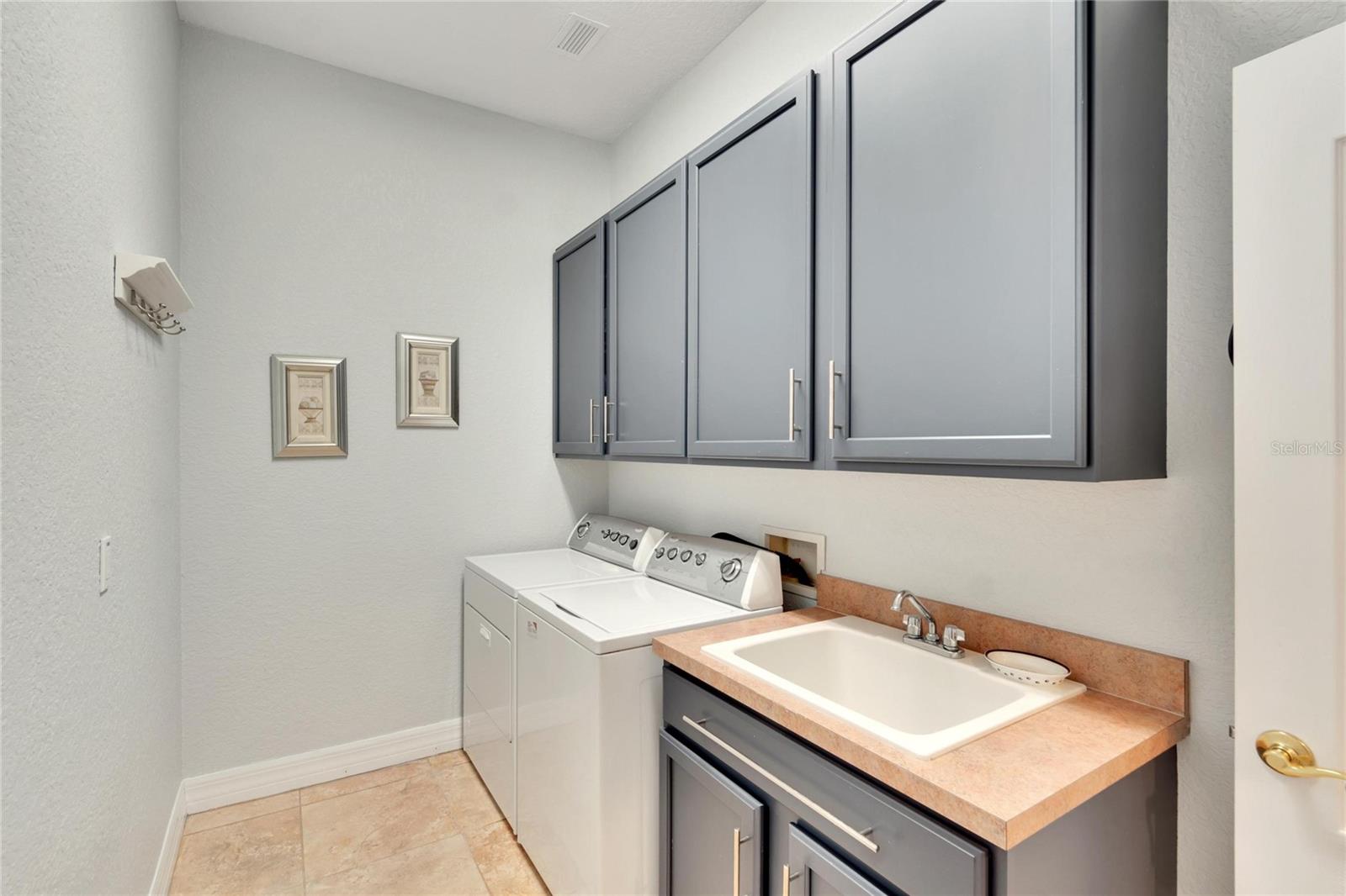Laundry Room with sink and tile flooring. Washer/Gas Dryer transfer upon sale. The Cabinet color is picked up in the kitchen island cabinet marrying the two rooms when the door is open.