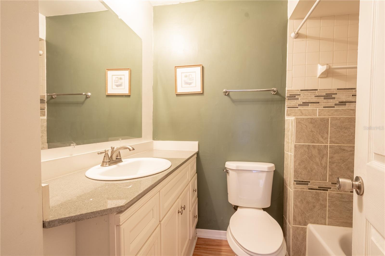 The bathroom features a tiled tub with a shower, a mirrored vanity with storage, and wood laminate flooring.