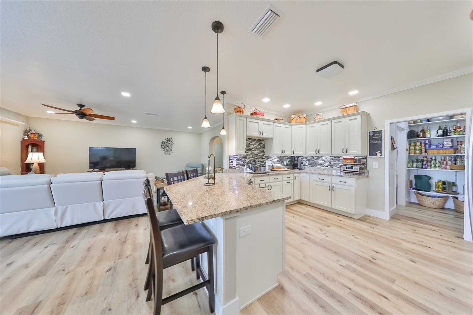 The kitchen has light colored floors to match the ivory colored cabinetry and neutral wall colors, and opens up into the oversized walk-in pantry room.