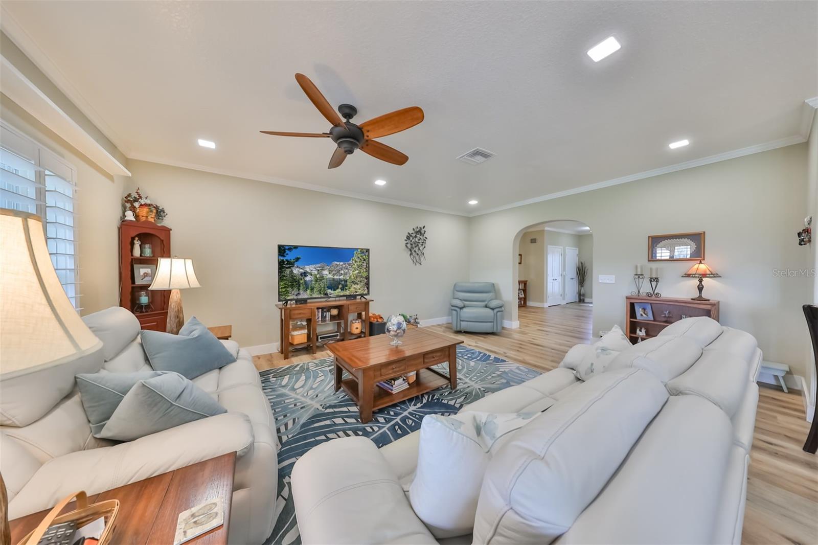 The great room feels contemporary and tranquil with soft tones, custom ceiling fan, high ceilings with crown molding, and recessed lighting for additional brightness.