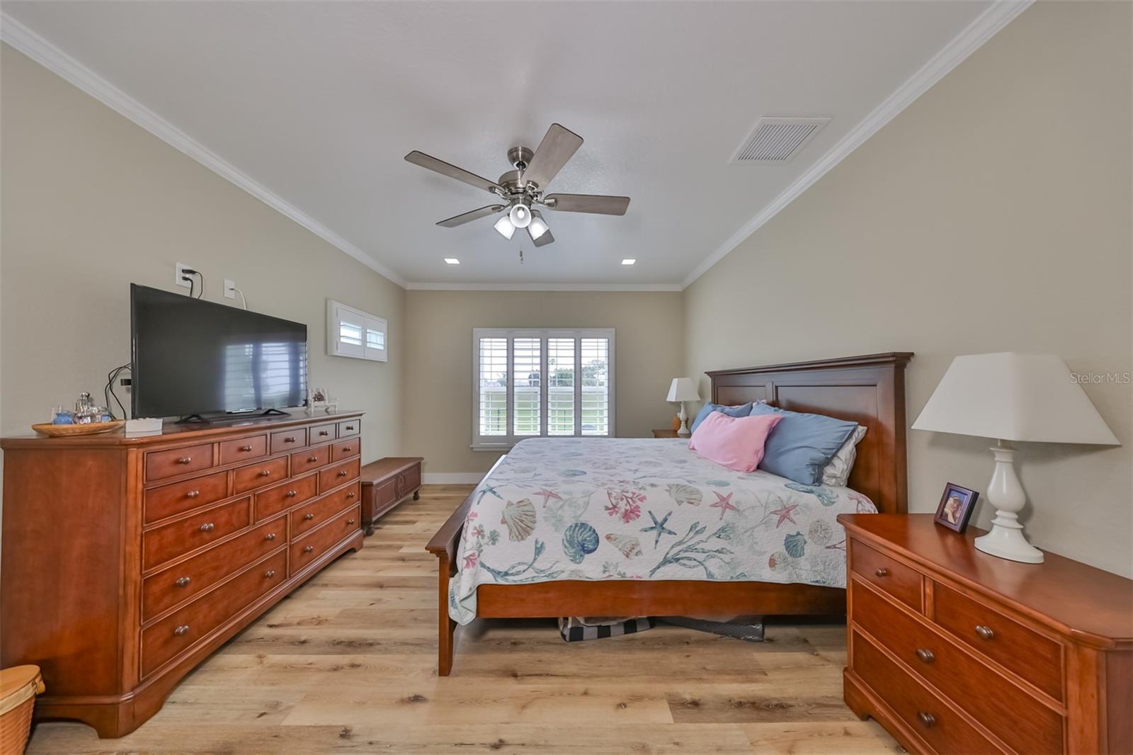 Primary bedroom with crown molding, plantation shutters and beautiful flooring.