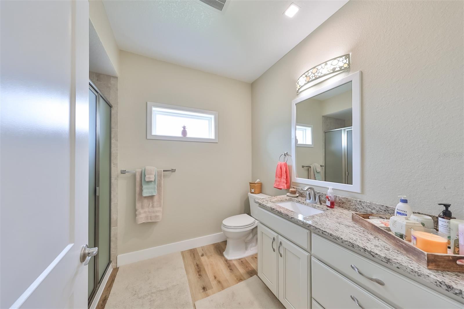 The guest bathroom includes recessed lighting, granite counters, matched flooring as throughout the home, and a walk in shower.
