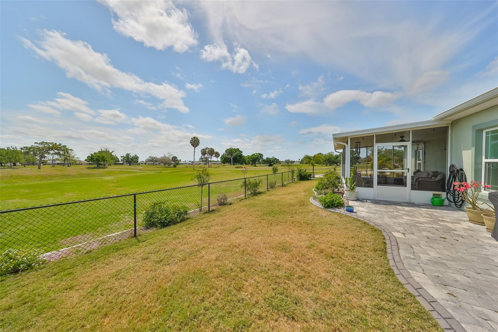Completely fenced in yard is perfect for pets. Notice the custom paved walkway and screened covered patio to relax and enjoy the view while golfers pass by.