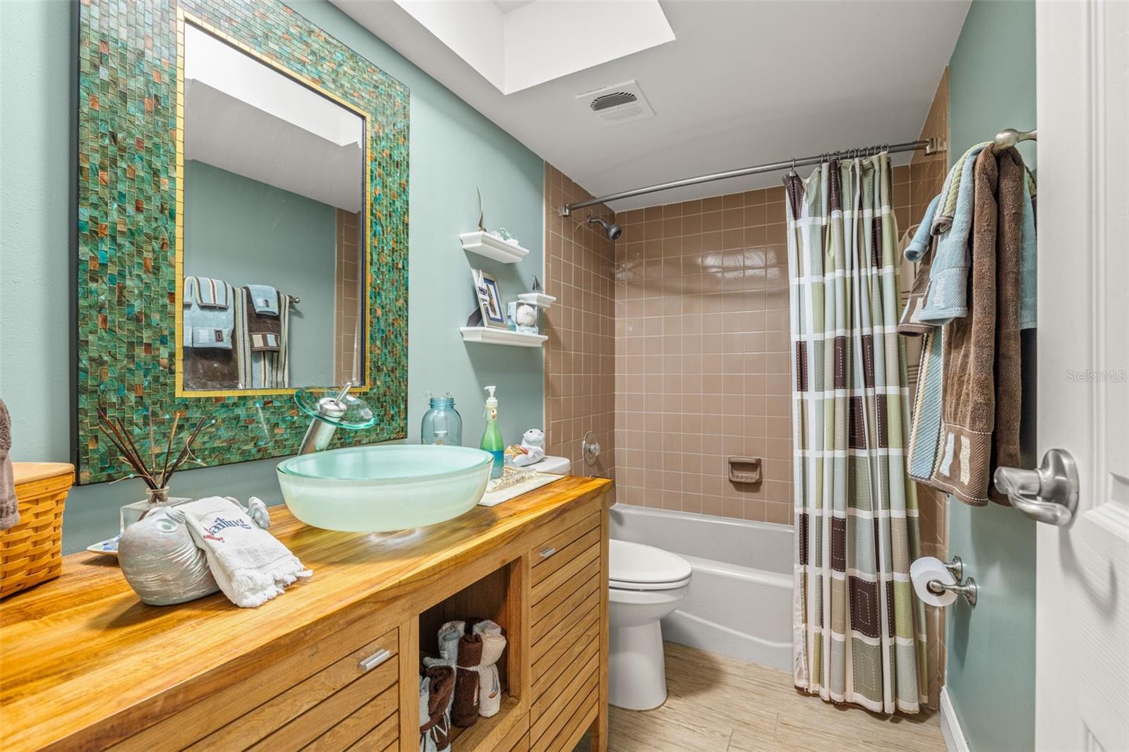 Updated secondary bathroom includes a fabulous teak vanity with waterfall sink basin, updated lighting, vanity mirror and flooring.