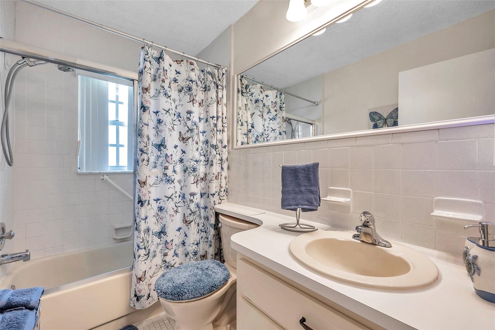 Guest bathroom has a tub with shower, window and single vanity.