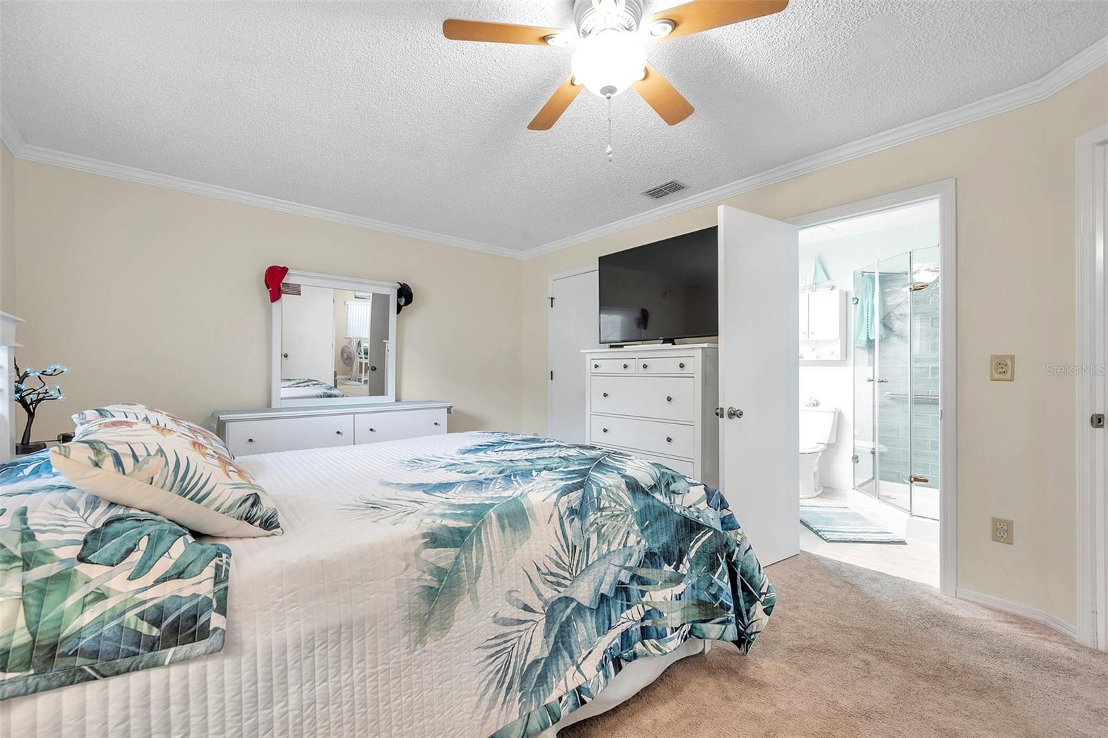 Primary bedroom has a ceiling fan with light, crown molding and neutral color paint.