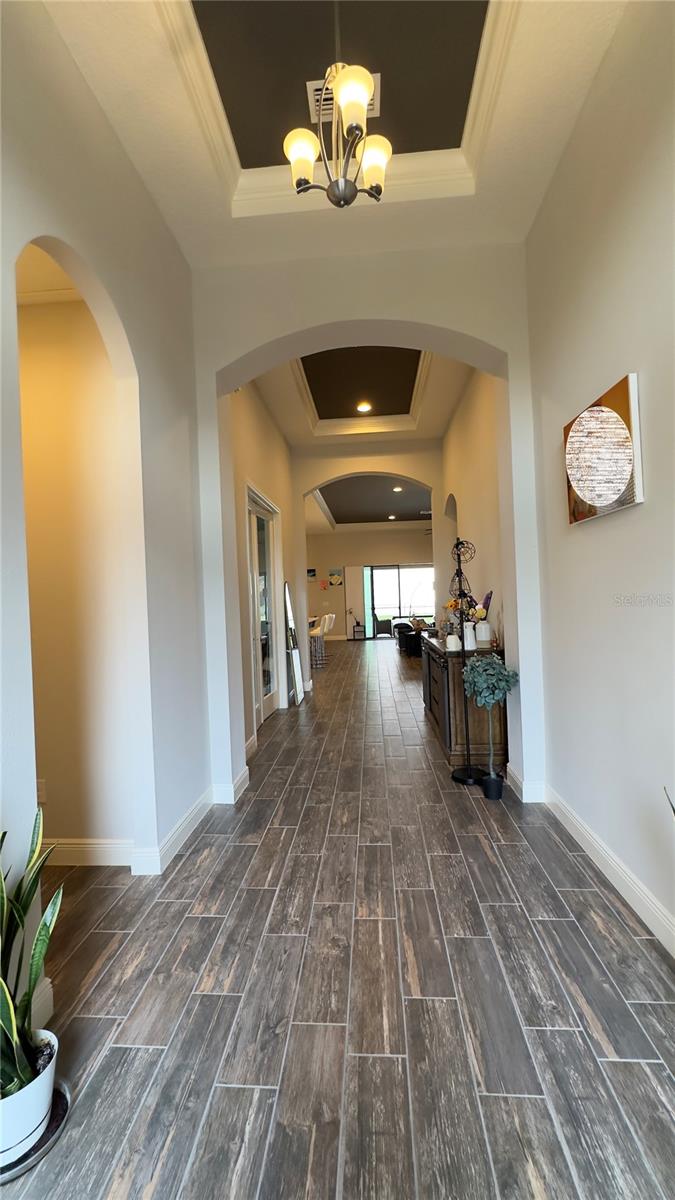 The long and elegant foyer grandly welcomes guests with its 12-ft tall, beautifully painted tray ceilingswith crown detail and luxurious wood-look ceramic tiles
