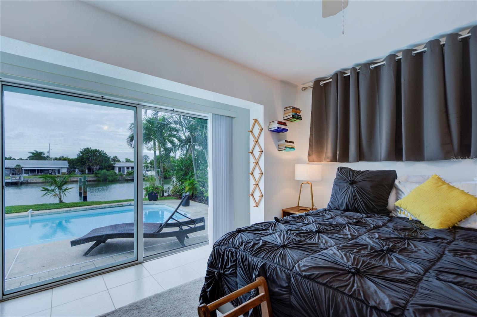 Primary bedroom with sliding glass door to pool and waterfront backyard.
