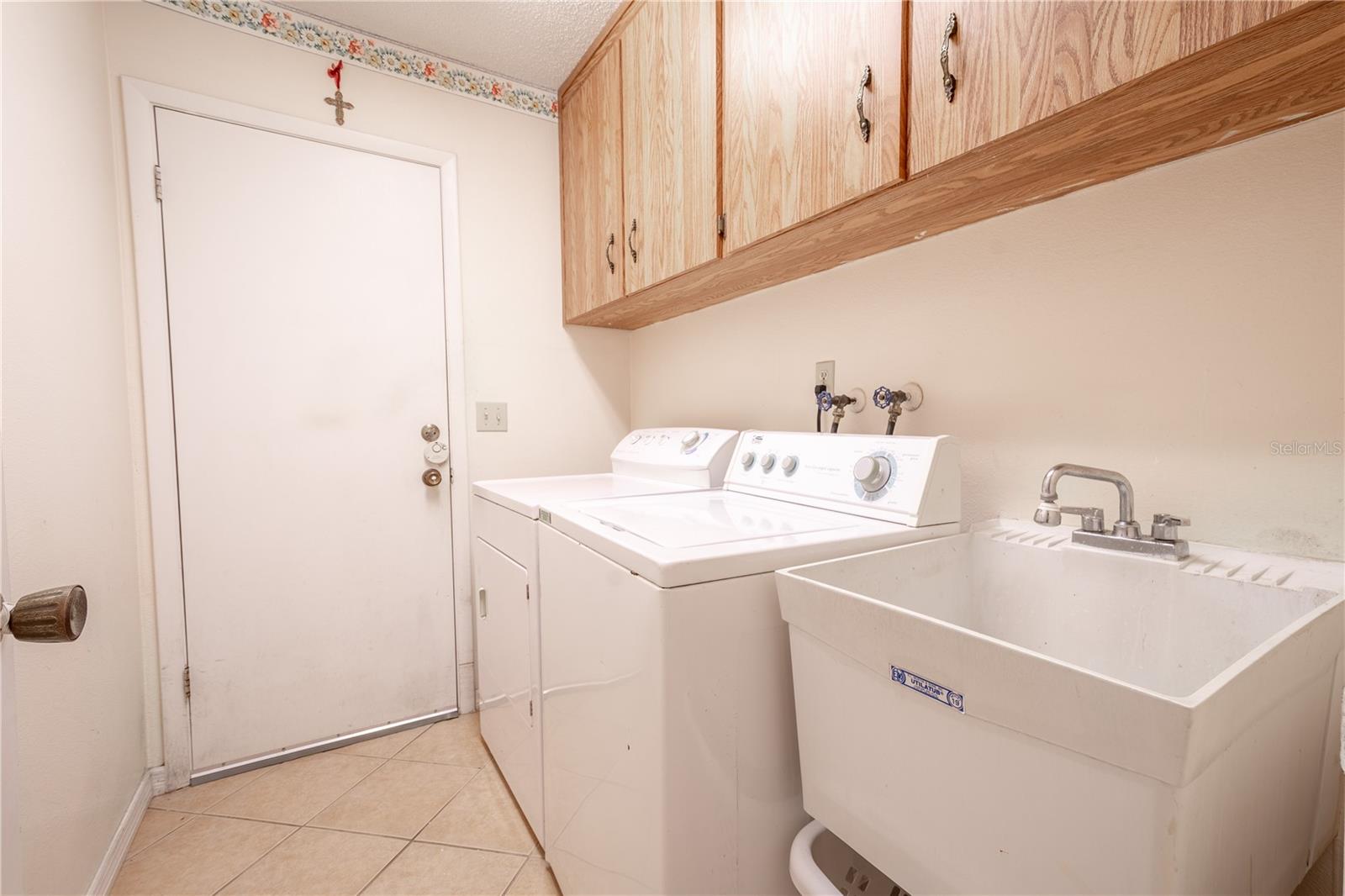 The laundry room features a washer and dryer, a utility sink, overhead storage cabinets and a door to access the garage.