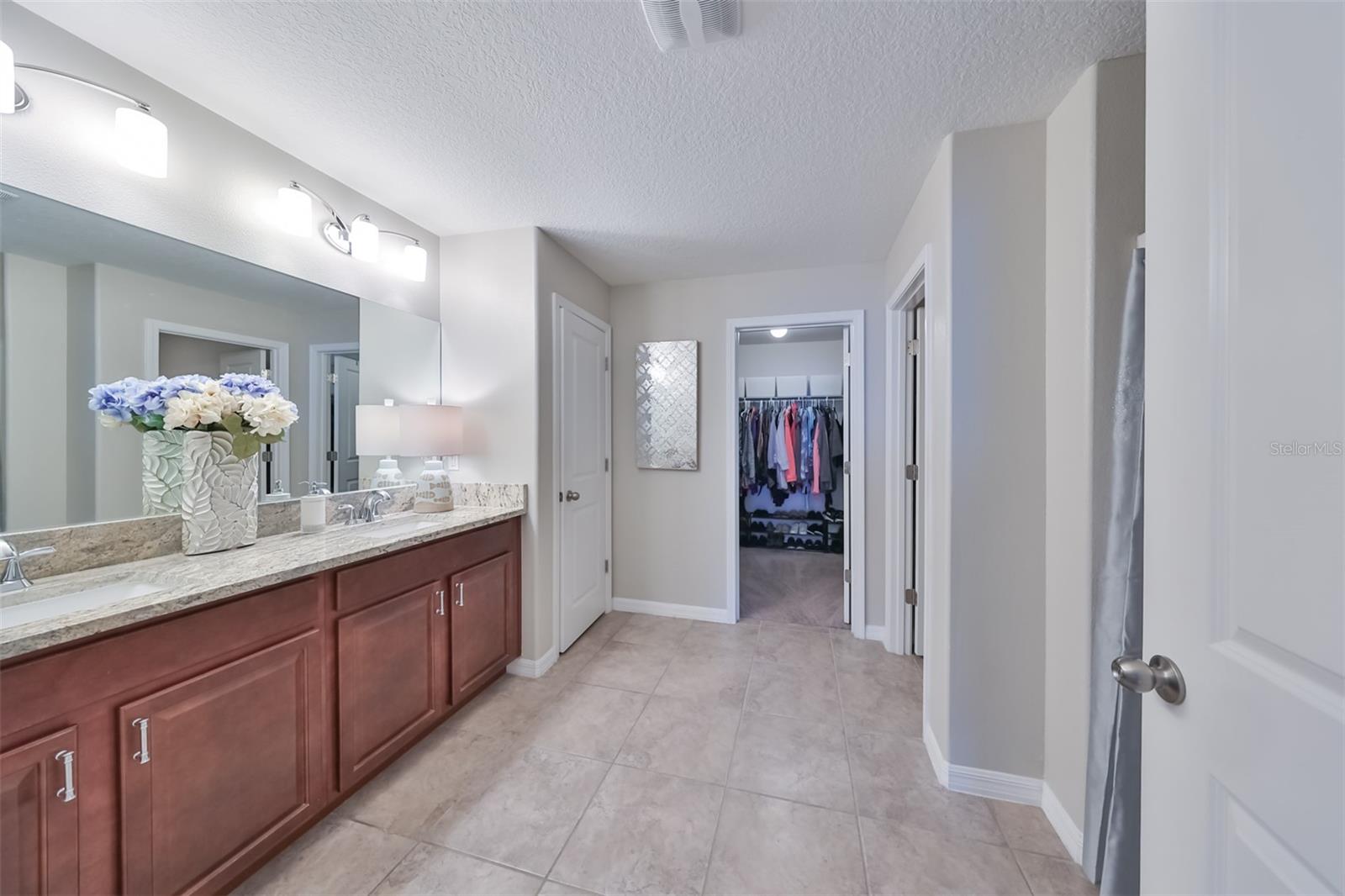 Large en-suite bathroom with walk-in closet, granite counters, private water closet and dual sinks is bright and inviting.