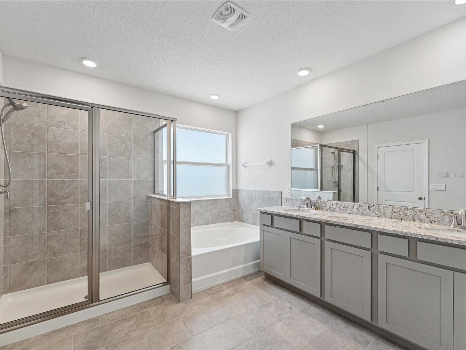 The ensuite bathroom consists of double sinks, cabinetry, shower with glass door, tub, and the second walk-in closet.