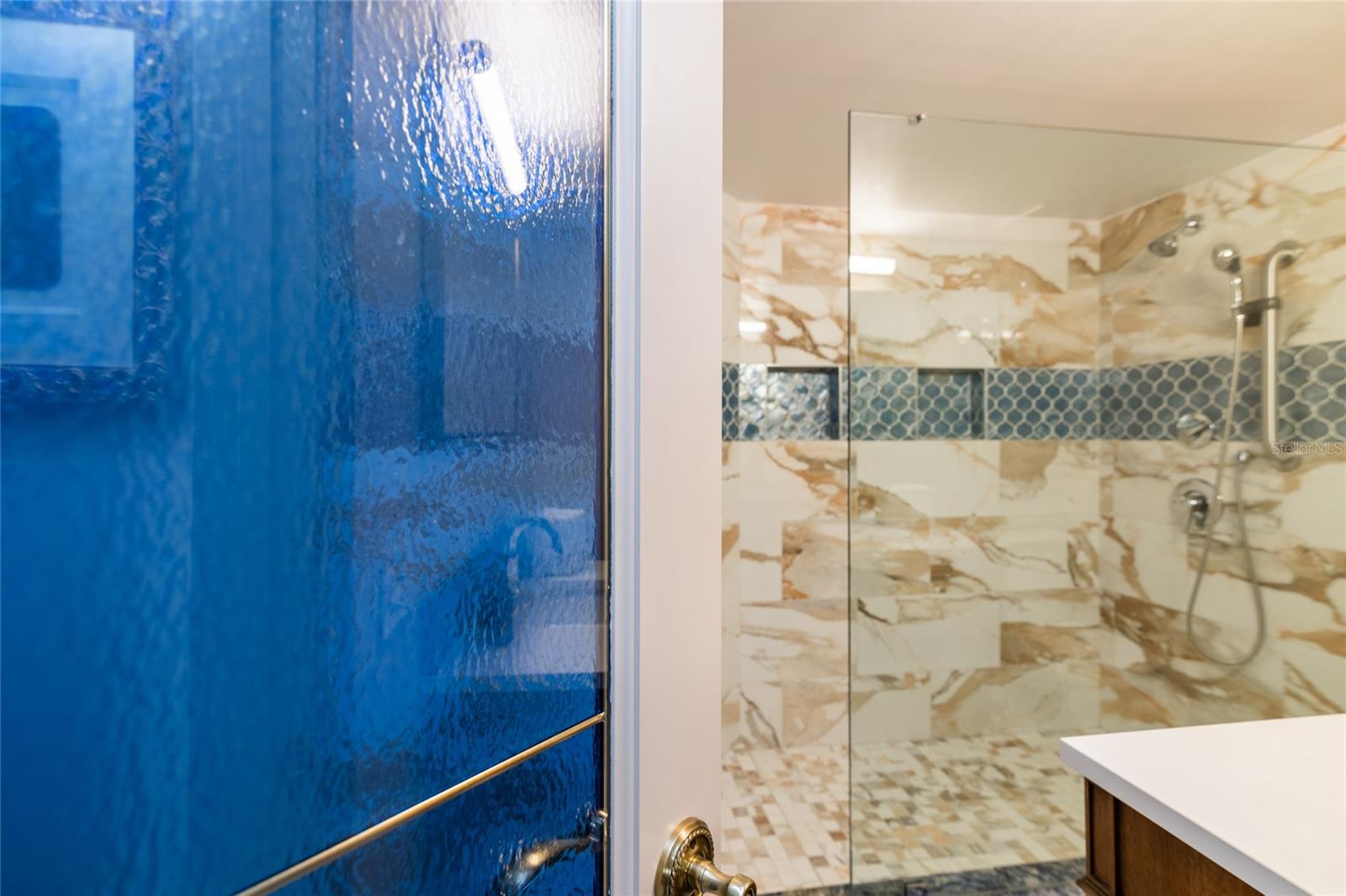 The guest bath has a frameless shower, custom tile work and a beautiful stain glass door.