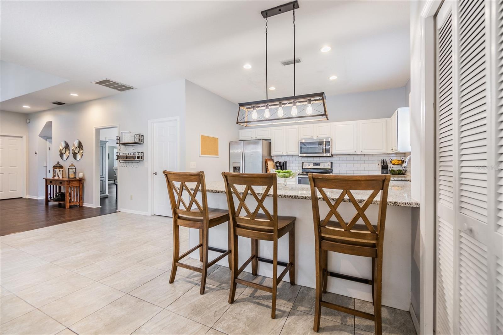 Large and Open kitchen with new light fixture, bar area, Granite Countertops, and Stainless Steel appliances.