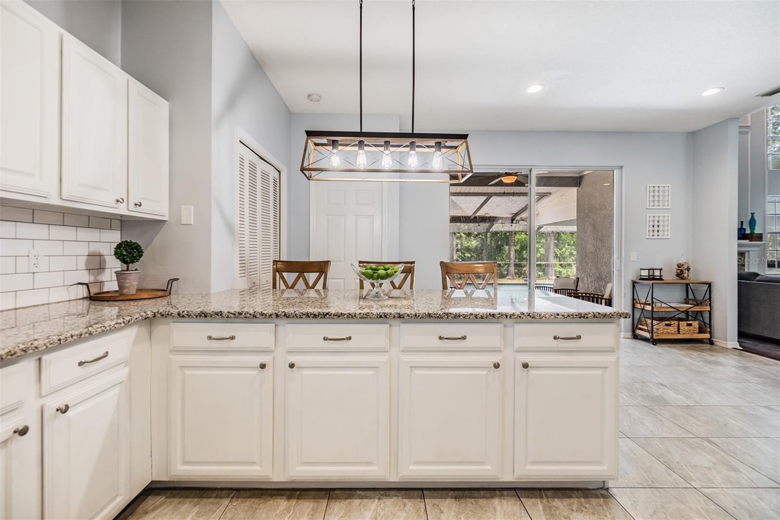 Large and Open kitchen with new light fixture, inset lighting, Subway Tile backsplash, Bar area, Granite Countertops, and Stainless Steel appliances.