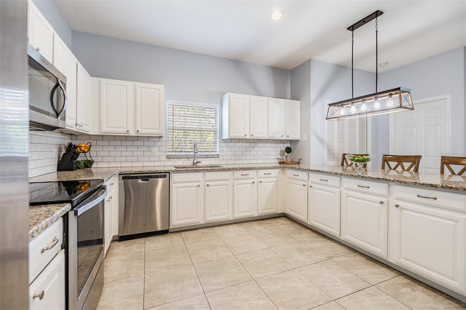 Large and Open kitchen with new light fixture, Subway tile backsplash, Granite Countertops, and Stainless Steel appliances.