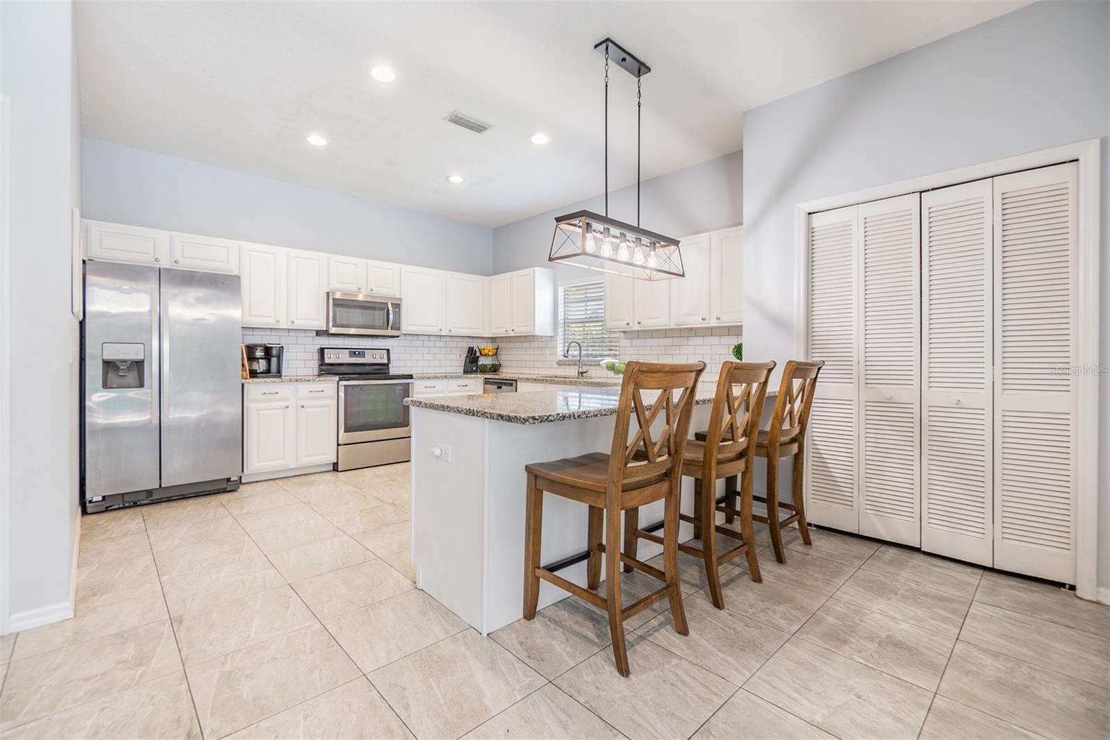 Large and Open kitchen with new light fixture, inset lighting,  Subway tile backsplash, Granite Countertops, and Stainless Steel appliances.