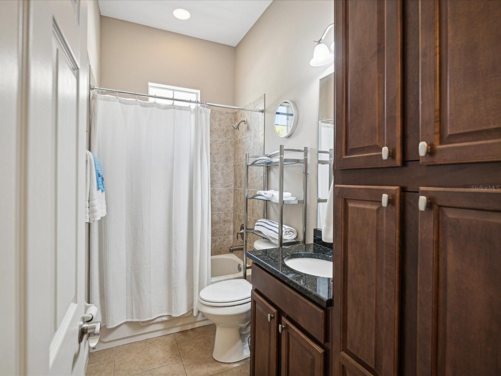 This bathtub shower combination includes granite counters and lots of built-in cherry cabinetry for storage.