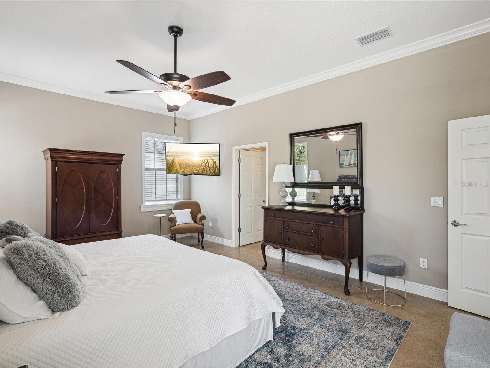 This bedroom features a ceiling fan with light, pull down window shades, and tile floors.