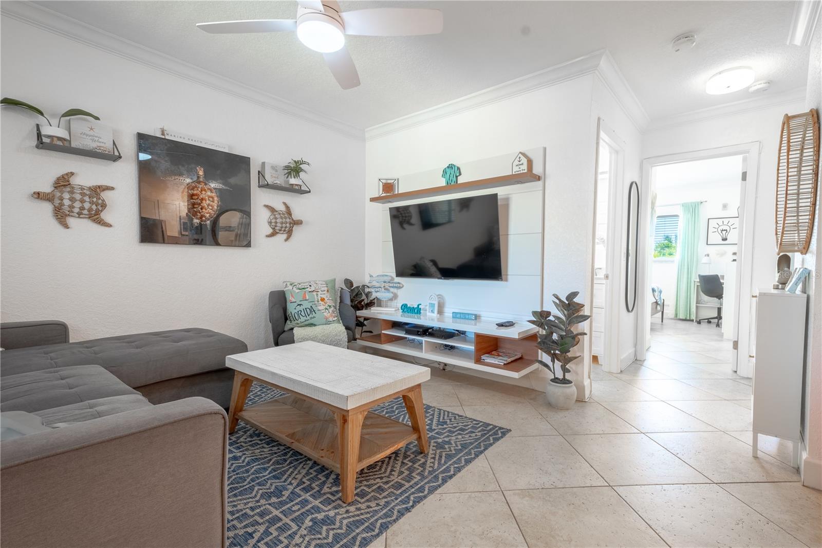 The living room features neutral tones, a beach vibe and a ceiling fan for year round comfort.