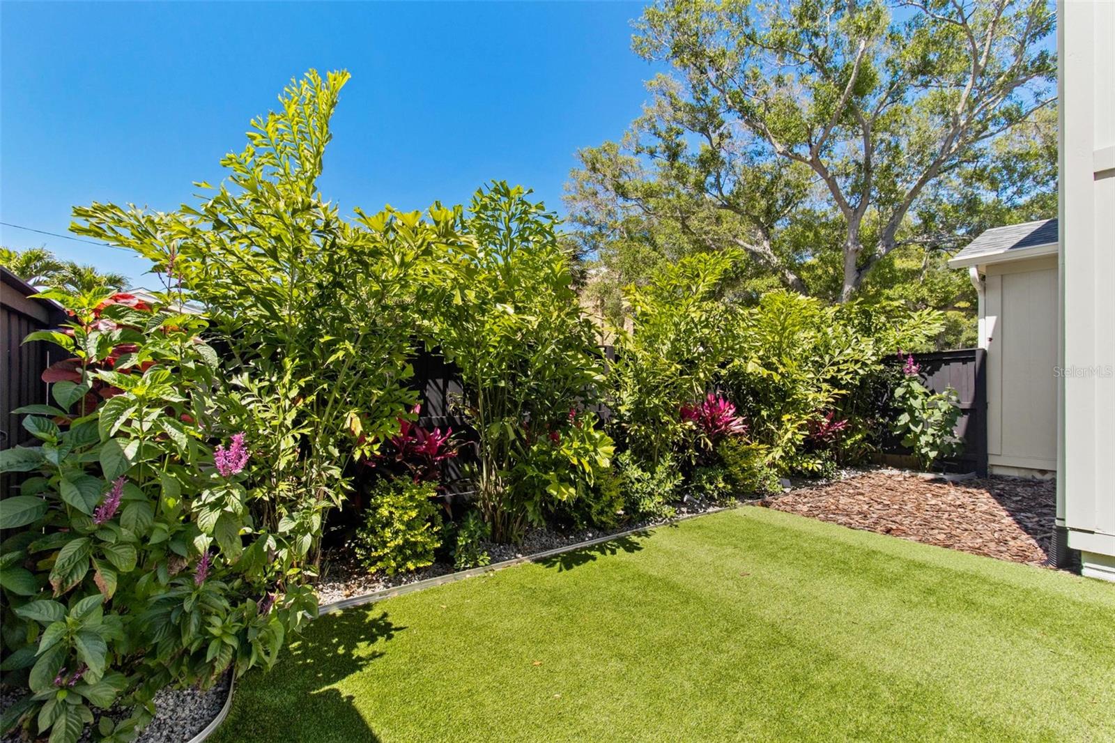Beautifully landscaped yard features natural tropical plants, artificial turf.