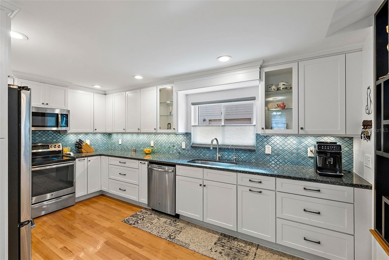 White shaker cabinetry with glass fronts, stone counters, chic backsplash, and recessed lighting.