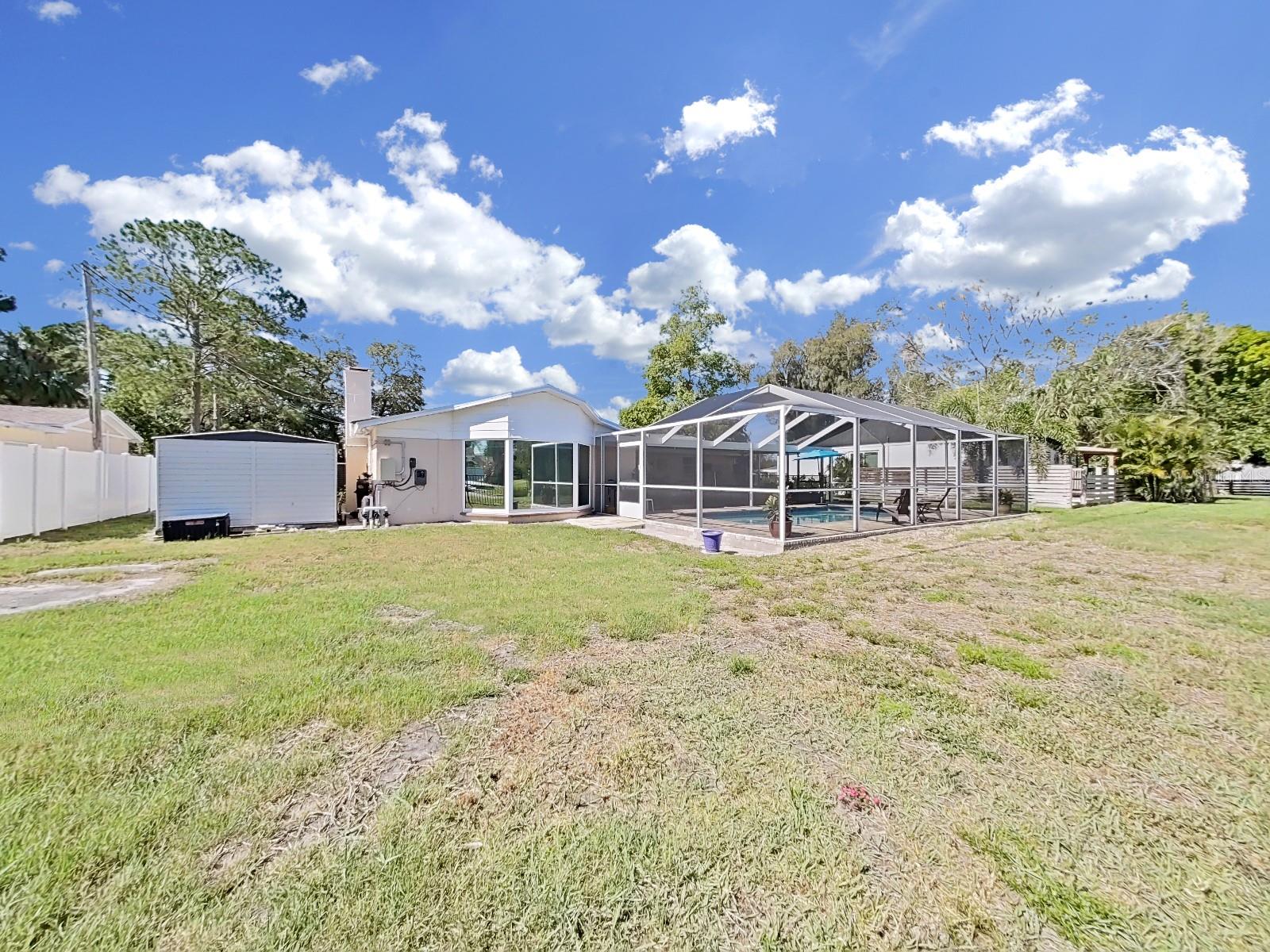 A view of the rear of the home, shed and pool area from the pond.