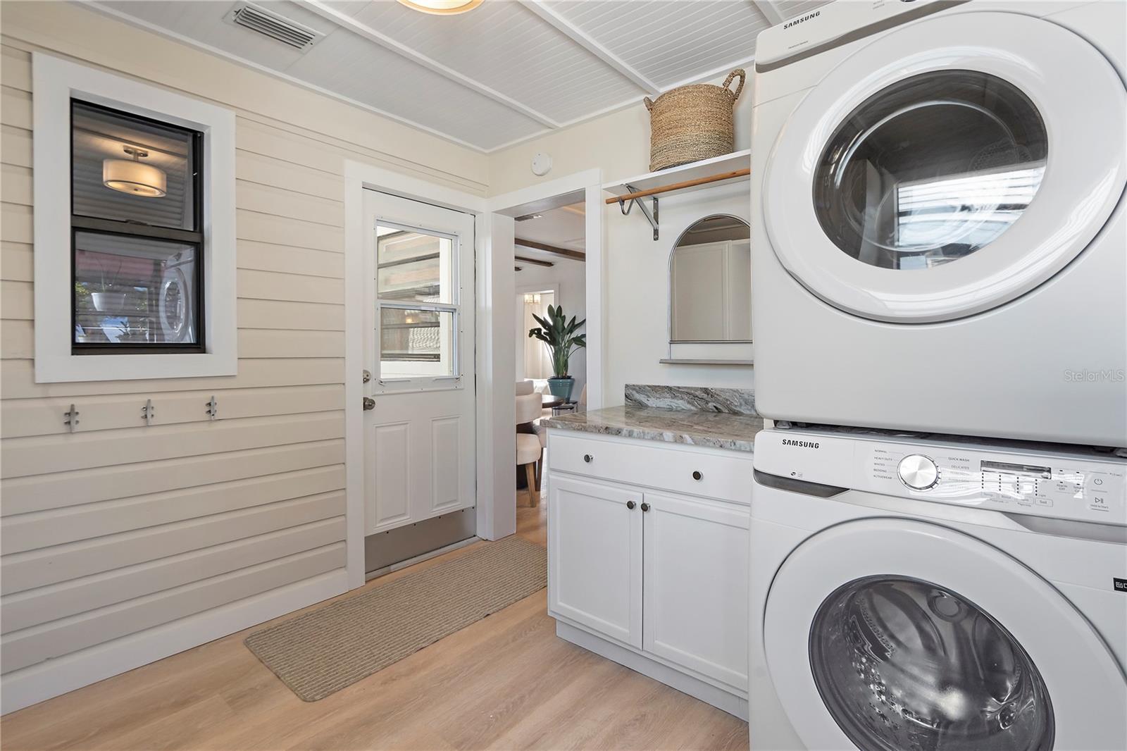 A large laundry and mudroom feature a Samsung stackable washer and dryer, with granite counter and cabinet with space to hang your clean laundry.
