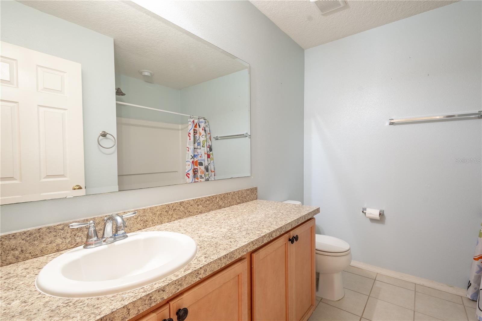 Bathroom three features a mirrored vanity with granite countertop and storage, a tub with shower and a ceramic tile floor.