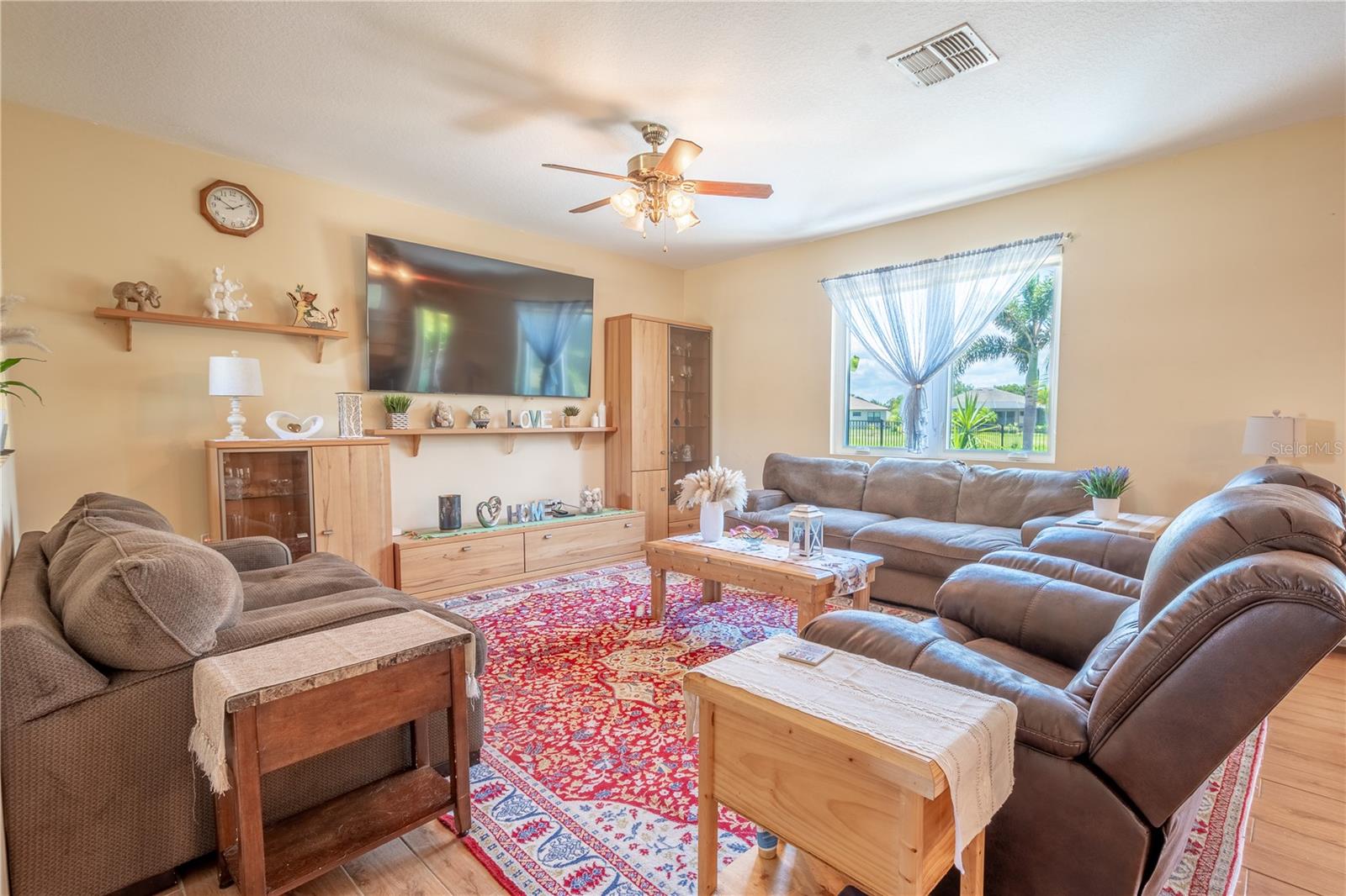 The living room features a picture window with a view of the tropical backyard, and a ceiling fan for year round comfort.