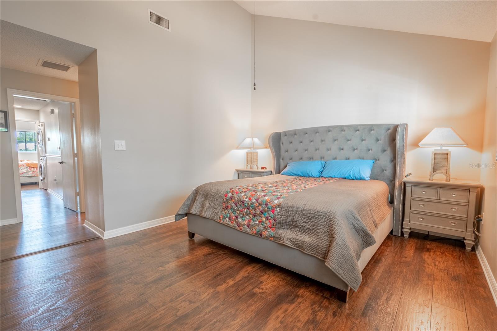 The primary bedroom features neutral tones, vinyl (wood plank) flooring and vaulted ceiling.