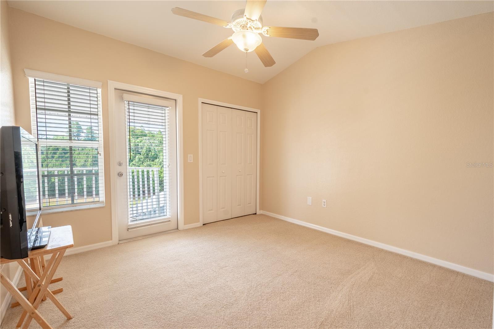 Bedroom 3 mirrors bedroom 2 with plush carpet, neutral tones, a ceiling fan, built in closet and French door to the shared balcony.